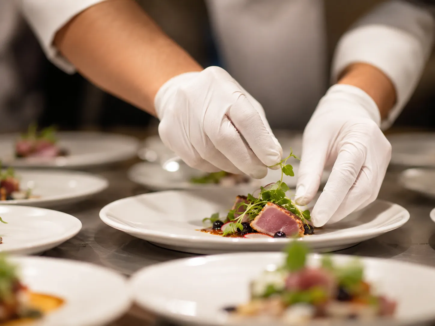 Personal de catering con guantes preparando alimentos higiénicamente